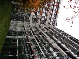 Blick von unten an einem hohen Fassadengerüst mit Belägen und Geländern entlang
