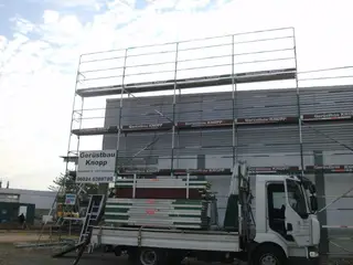 Gerüst-Lkw mit Gerüstmaterial vor einem Fassadengerüst