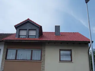 Schieferverkleidete Gaube auf einem roten Ziegeldach